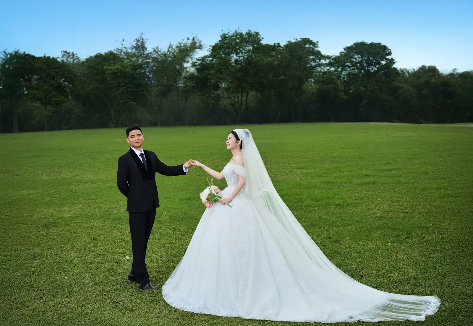 Cô dâu chú rể nắm tay trên thảm cỏ